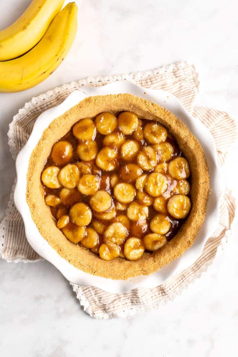 A graham cracker crust topped with caramelized bananas against white background
