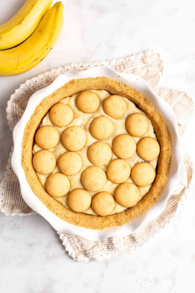 Nilla wafers being topped on banana cream for a banana pudding pie