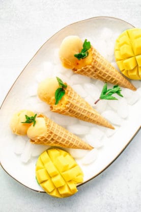 Three ice cream cones filled with mango ice cream on a tray filled with ice