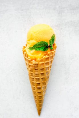 One mango sorbet filled ice cream cone with a sprig of mint