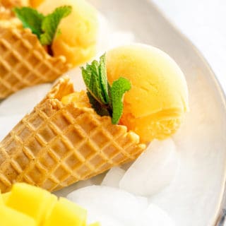 A close up of mango sorbet cones with mint and fresh mango on ice in a tray