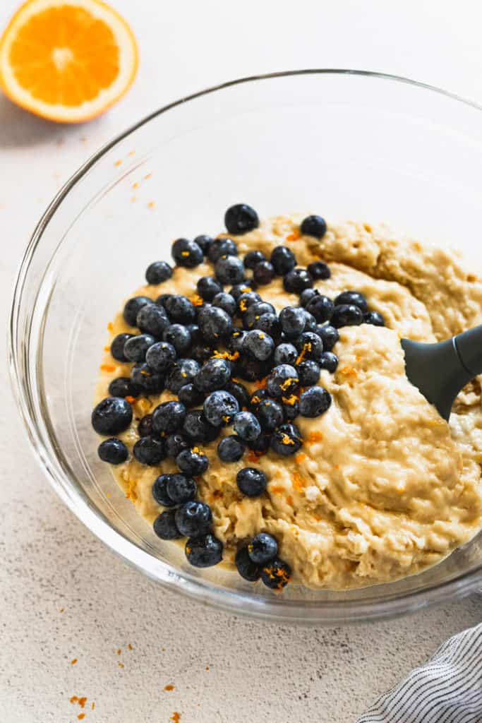 Muffin batter being mixed with blueberries and orange zest tossed in