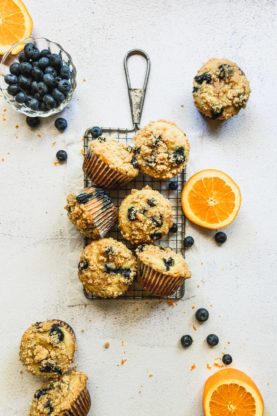 A beautiful display of orange blueberry muffins scattered over a serving wire rack with sliced oranges and blueberries
