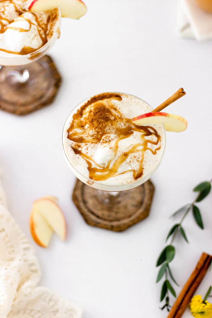 An overhead shot of apple cider floats in wine glasses ready to serve with apple slices on the background