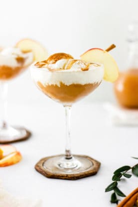 Two wine glasses filled with apple cider floats with apple cider in the white background