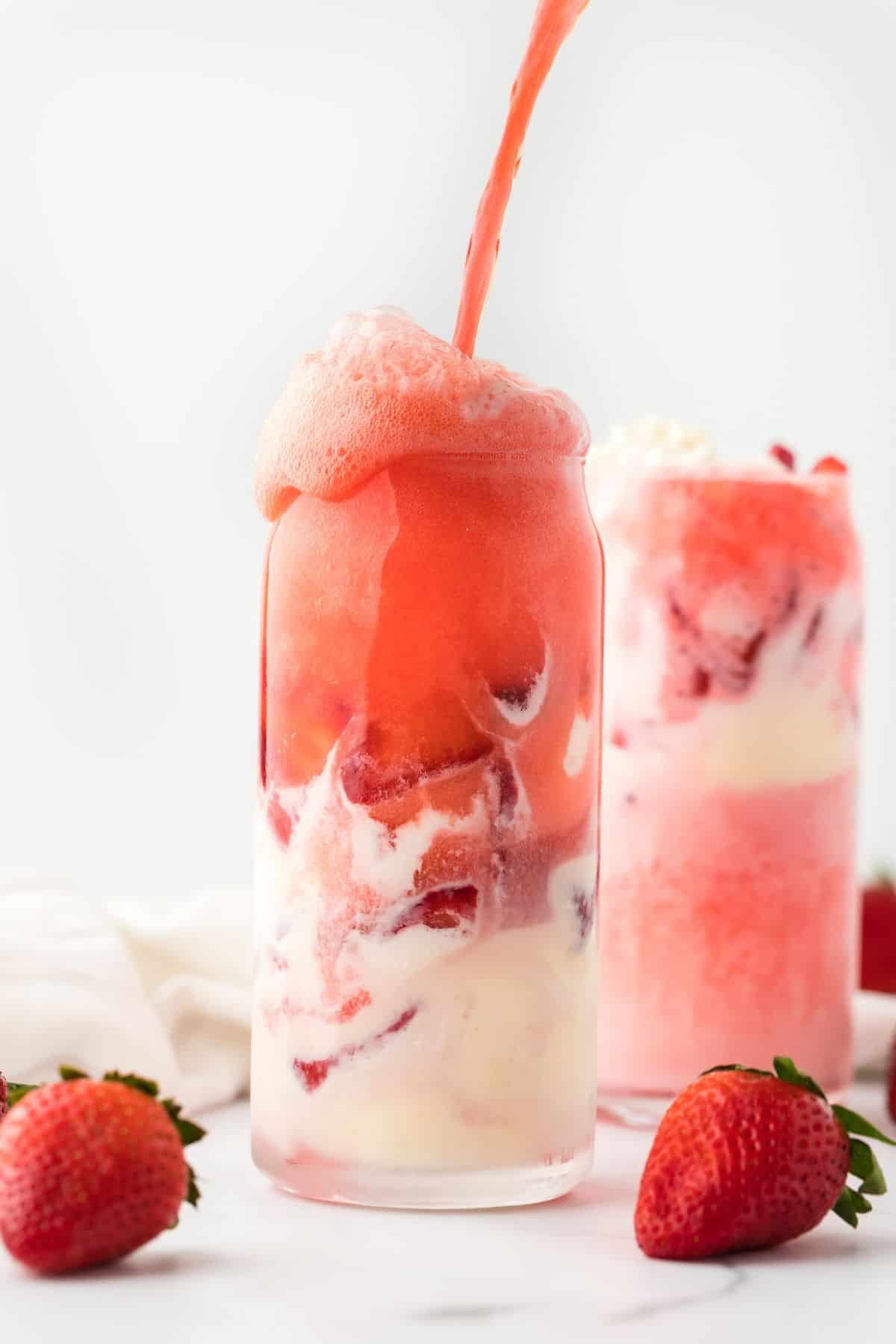 A strawberry float on the table with liquid pouring into the glass from the top. 