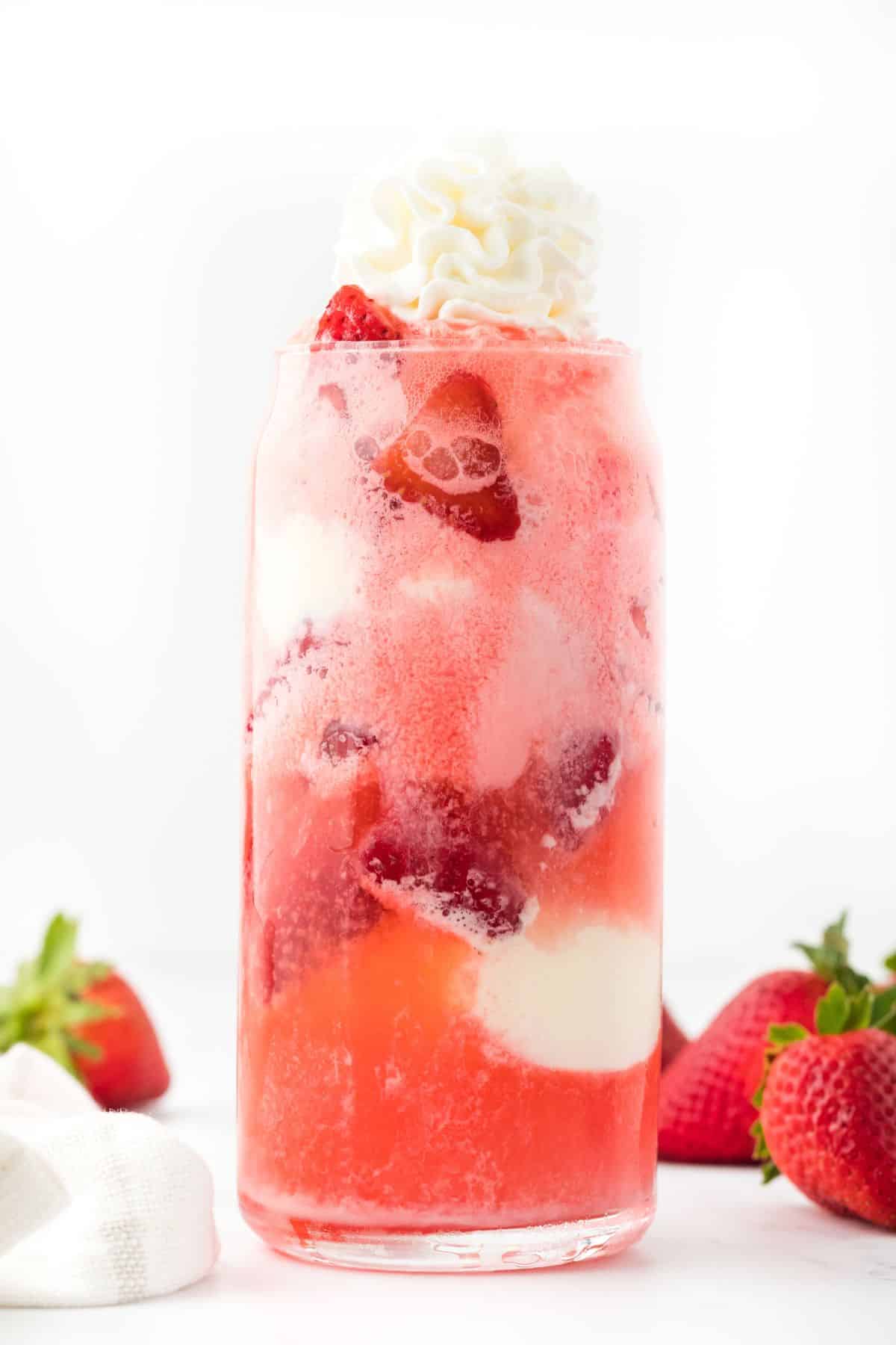 A strawberry float on a table surrounded by whole strawberries.