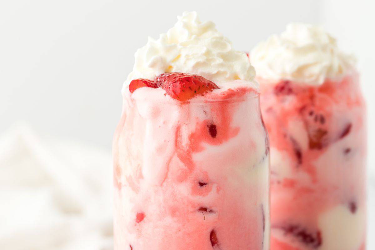 Two glasses of strawberry floats on the table topped with whipped cream.