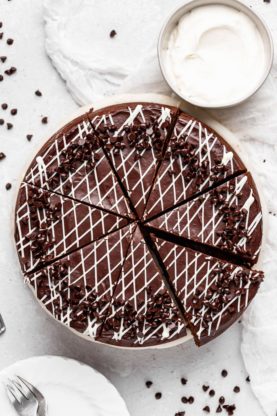 An overhead of a chocolate and white chocolate cheesecake with slices cut and ready to serve against a white background