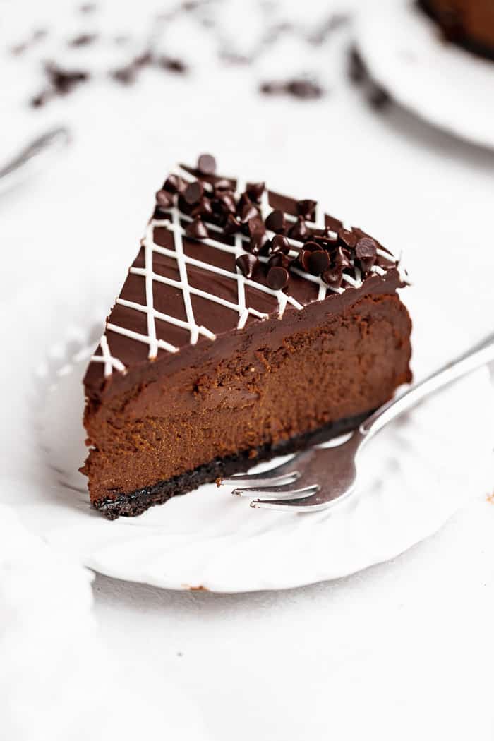 A slice of deep chocolate cheesecake on a white plate with a fun design ready to serve