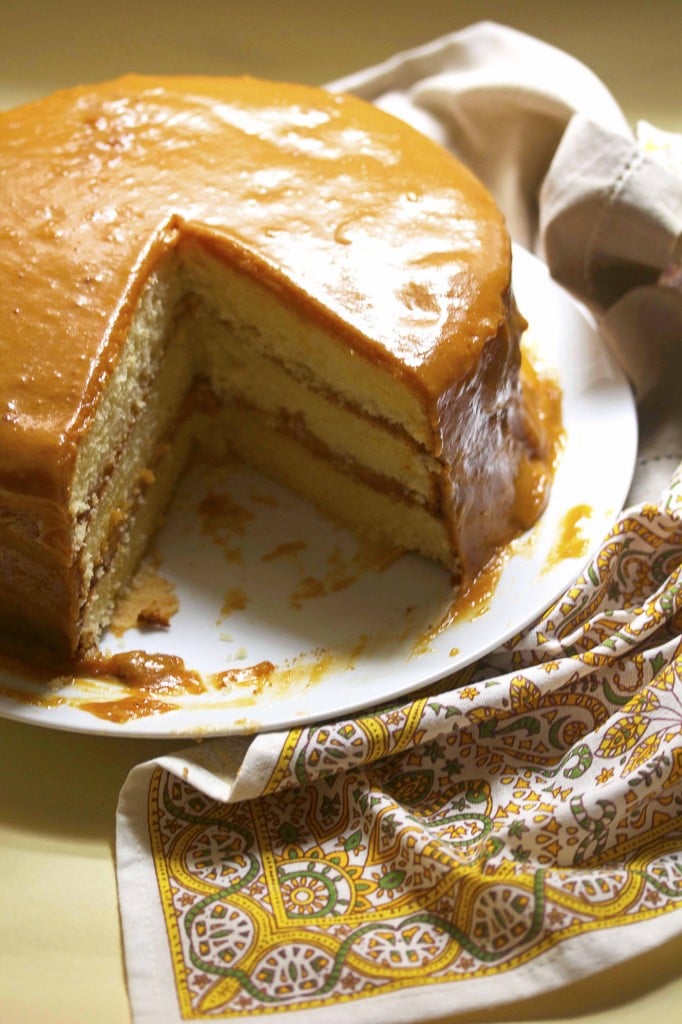 A 3-Layer Caramel Cake with a Slice Missing on a White Plate