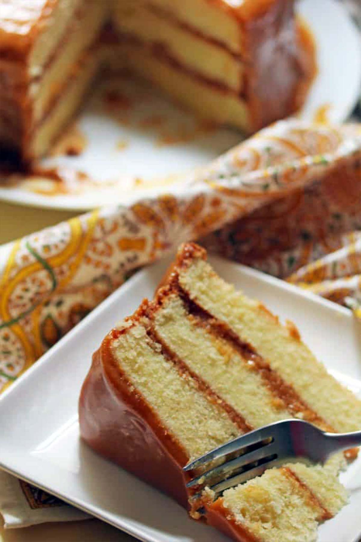 A slice of southern caramel cake with a fork cutting a bite.