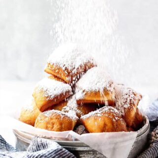 New Orleans beignets in a basket with powdered sugar sprinkled over top.