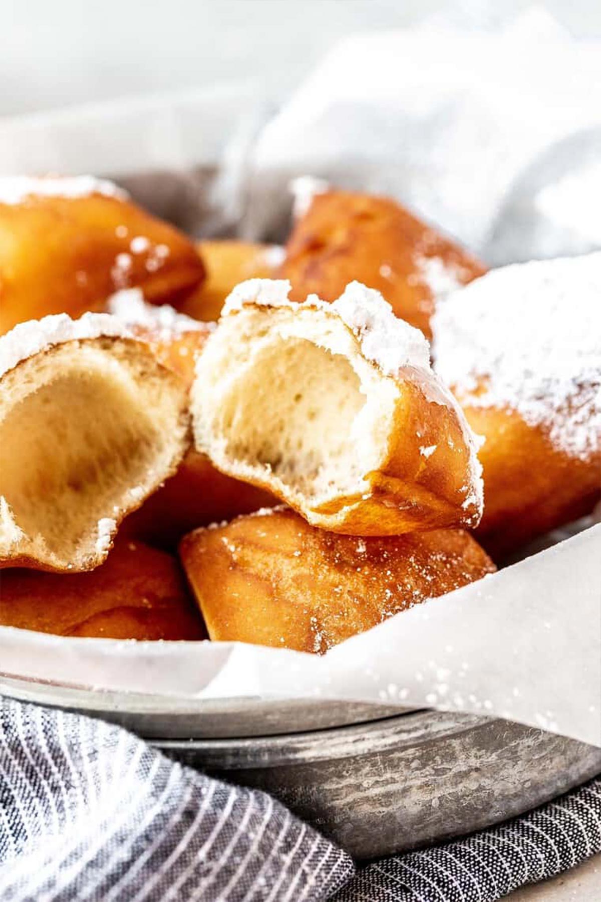 A close up of New Orleans beignets with one broken apart to show inside.