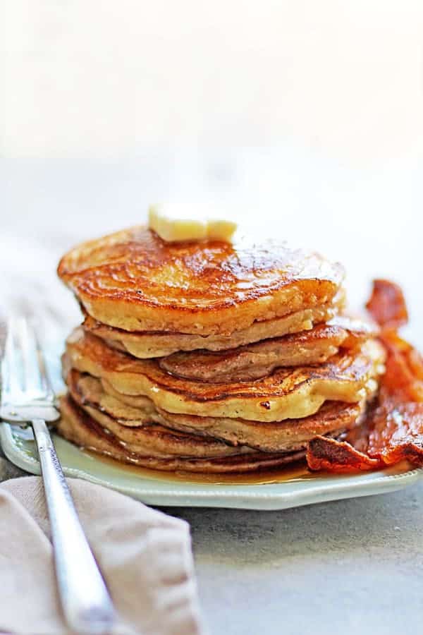 Best Classic Pancakes topped with butter and sitting next to a strip of bacon and a fork