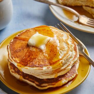 A stack of fluffy pancakes on a plate with maple syrup and butter on top.