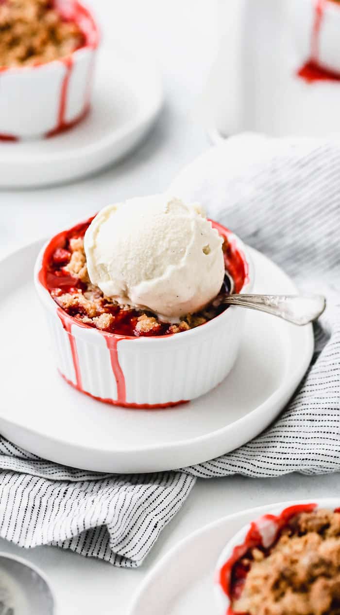 Individual Strawberry Crumble topped with one scoop of vanilla ice cream and a spoon
