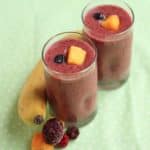 Mango banana berry smoothie contained in two glasses and topped with mango and blueberries
