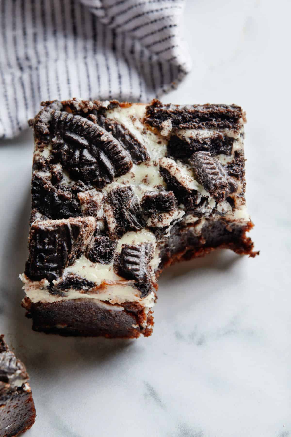 Oreo brownie with cheesecake top with a bite missing sitting directly on the counter.