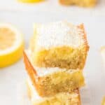 A stack of three lemon brownies on the table dusted with powdered sugar.