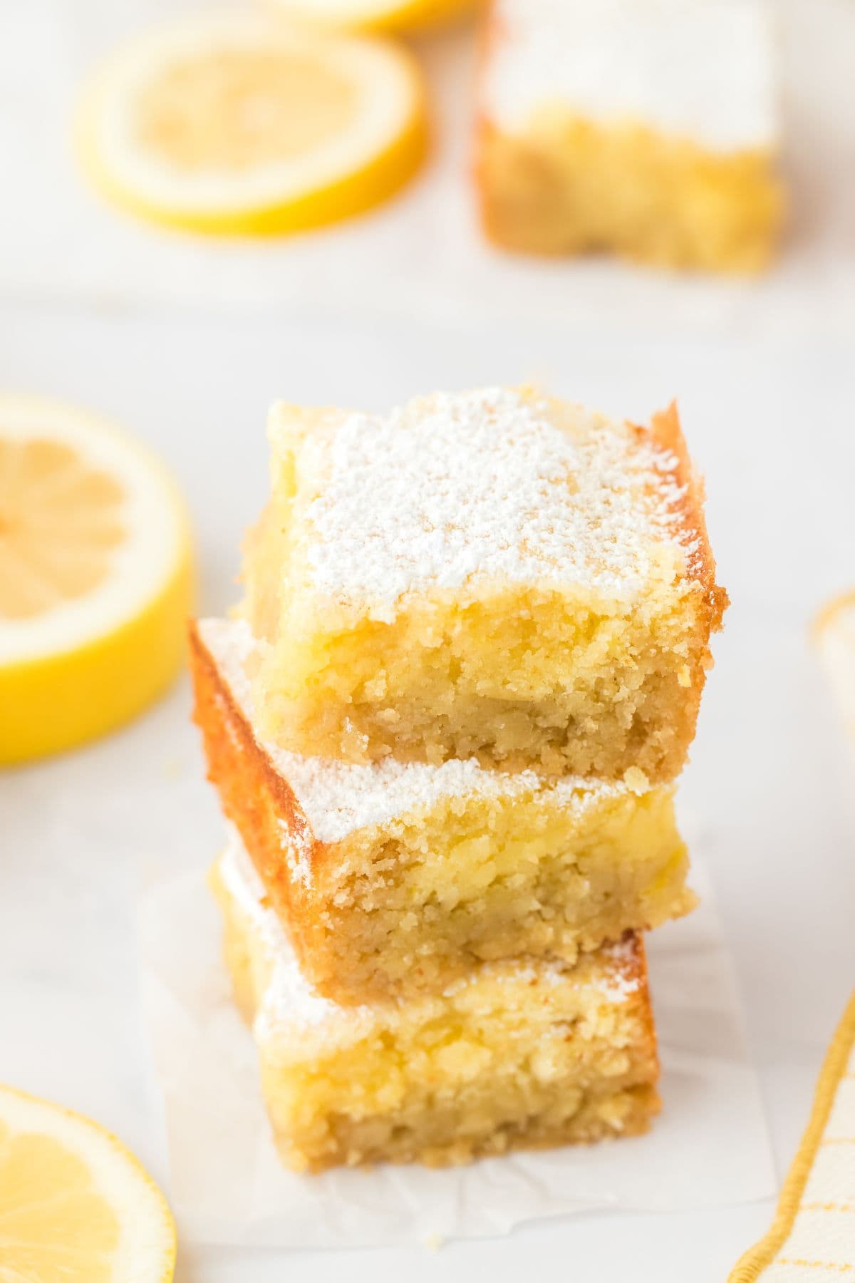 A stack of three lemon brownies on the table dusted with powdered sugar.