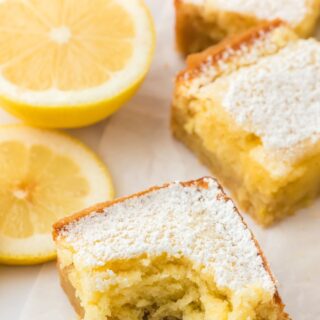 Lemon brownies cut into squares on the table with one in front missing a bite.