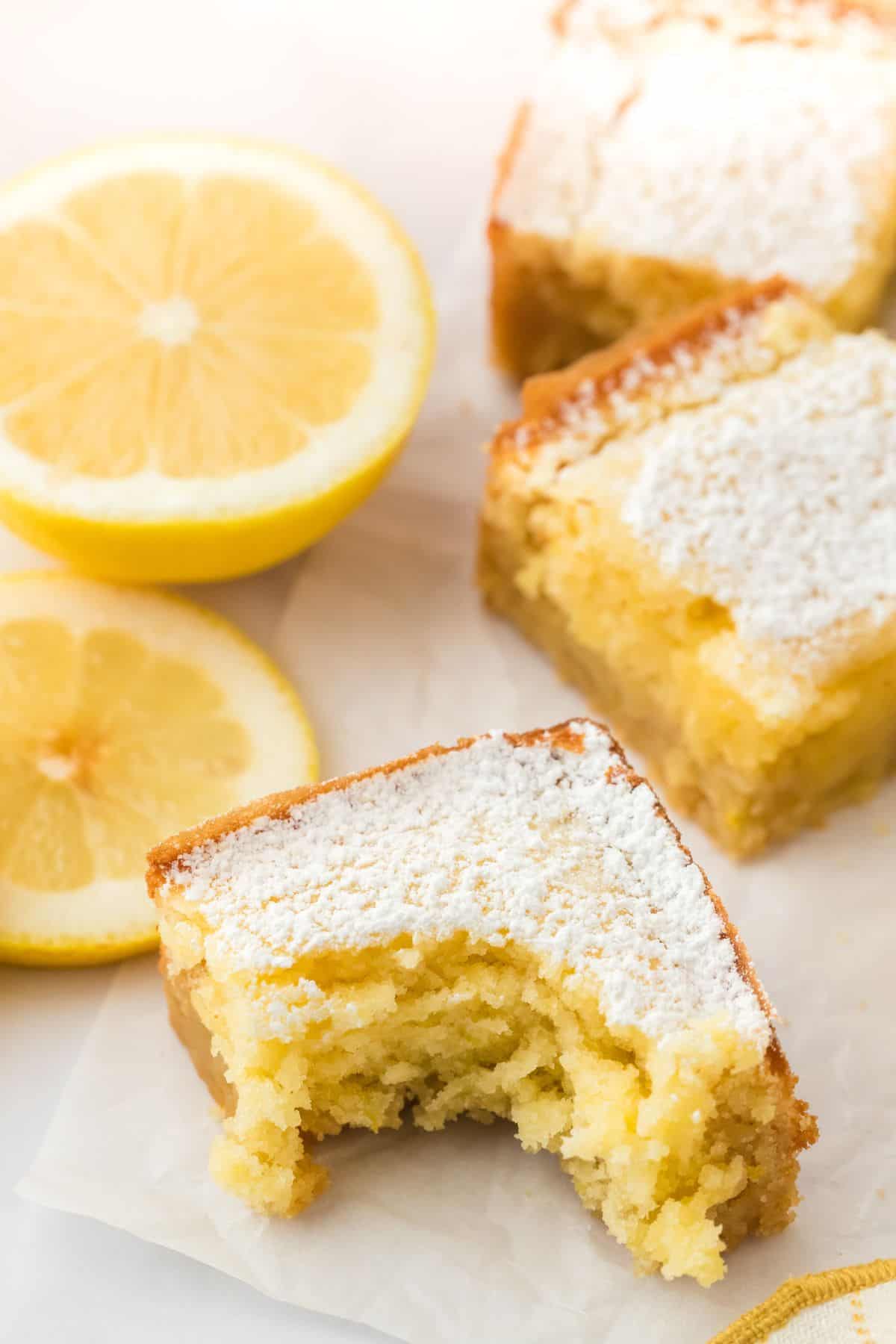 Lemon brownies cut into squares on the table with one in front missing a bite.
