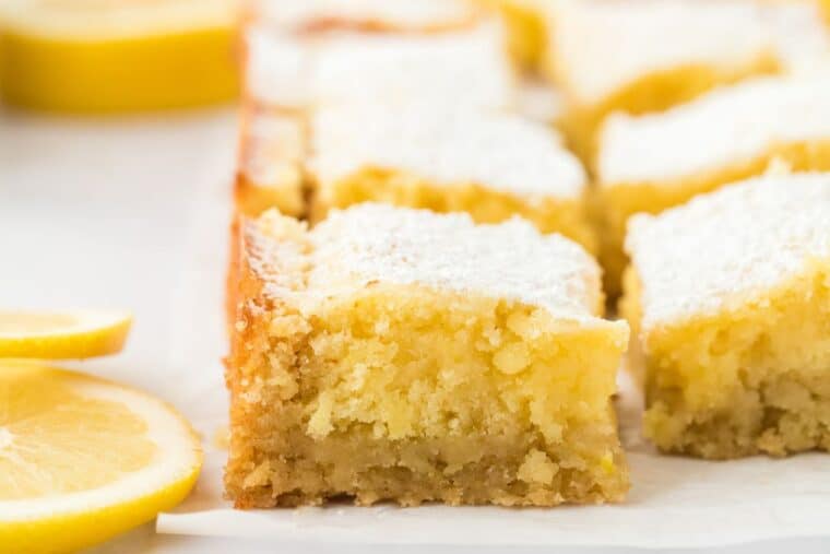 A side view of lemon flavored brownies with lemon slices on the table cut into squares.