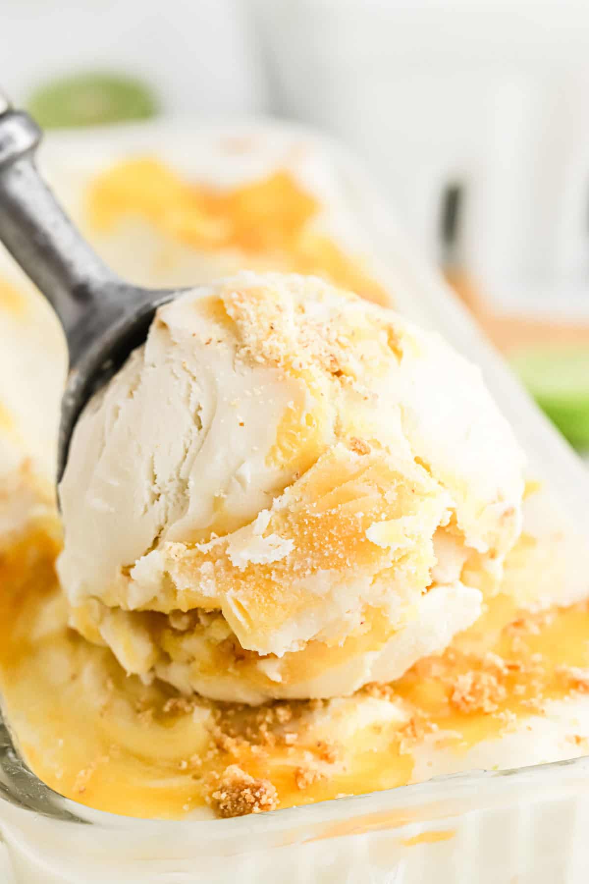 Scoop of key lime ice cream on top of container showing mango puree swirl.