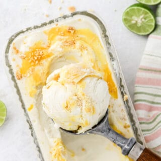 Key lime ice cream with a scoop in the ice cream scoop on top of container of key lime pie ice cream.
