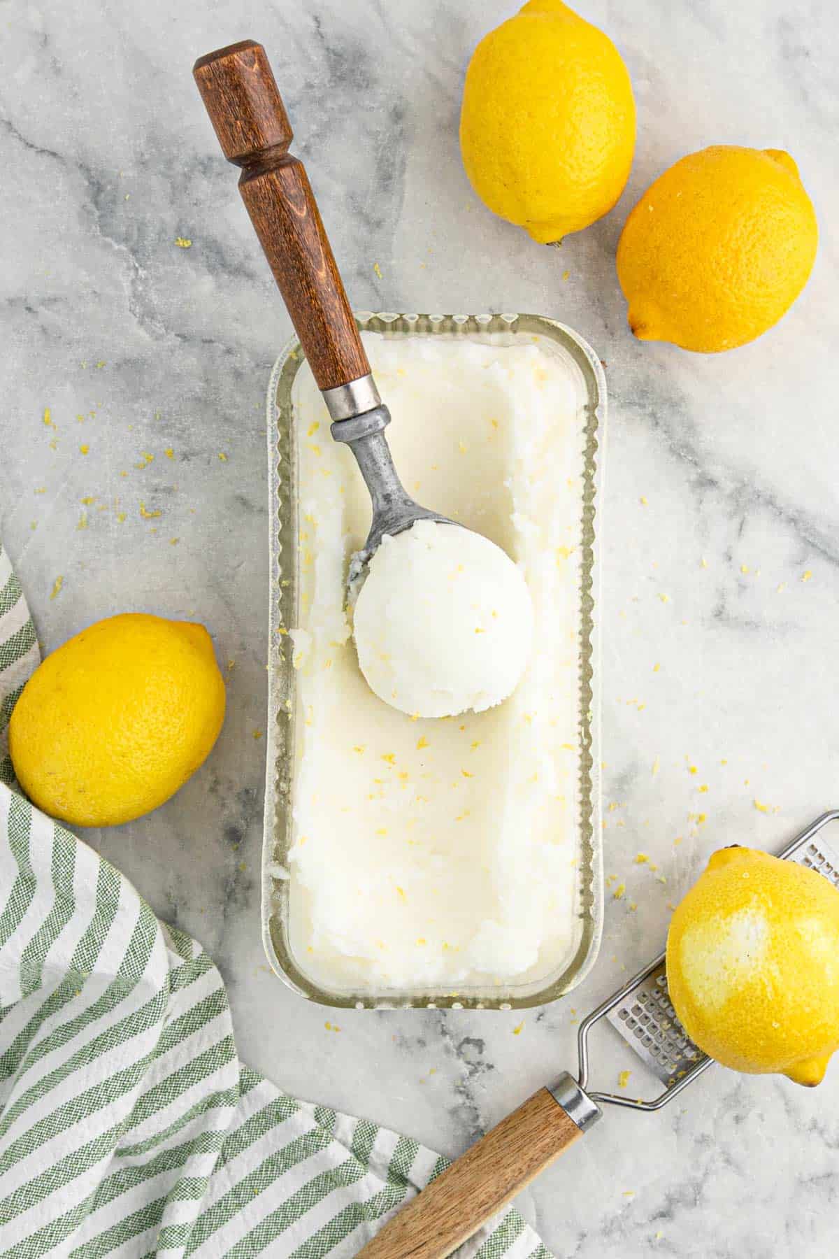 Overhead of lemonade sorbet in a container with a ice cream scoop on top filled with sorbet.
