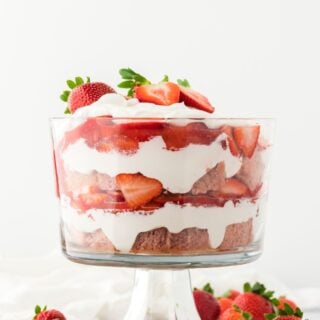 A strawberry shortcake trifle in a glass bowl with a white background and berries surrounding it