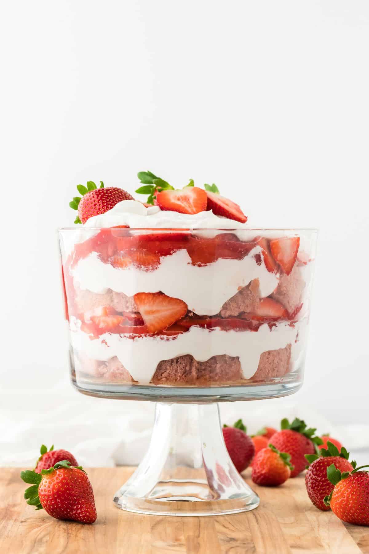 A strawberry trifle in a glass bowl showing the layers and topped with whipped cream and fresh berries.