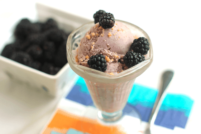 Blackberry Crumble Ice Cream contained in a glass and topped with fresh blackberries and a basket of blackberries in the background and out of focus.