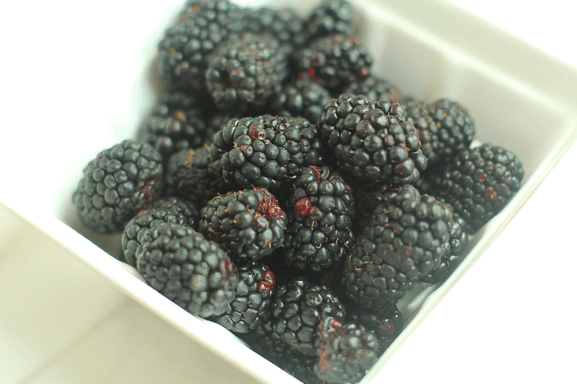 Close up of a white basket containing fresh blackberries.