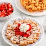 Funnel cake served up sprinkled with powdered sugar, whipped cream and fresh berries.
