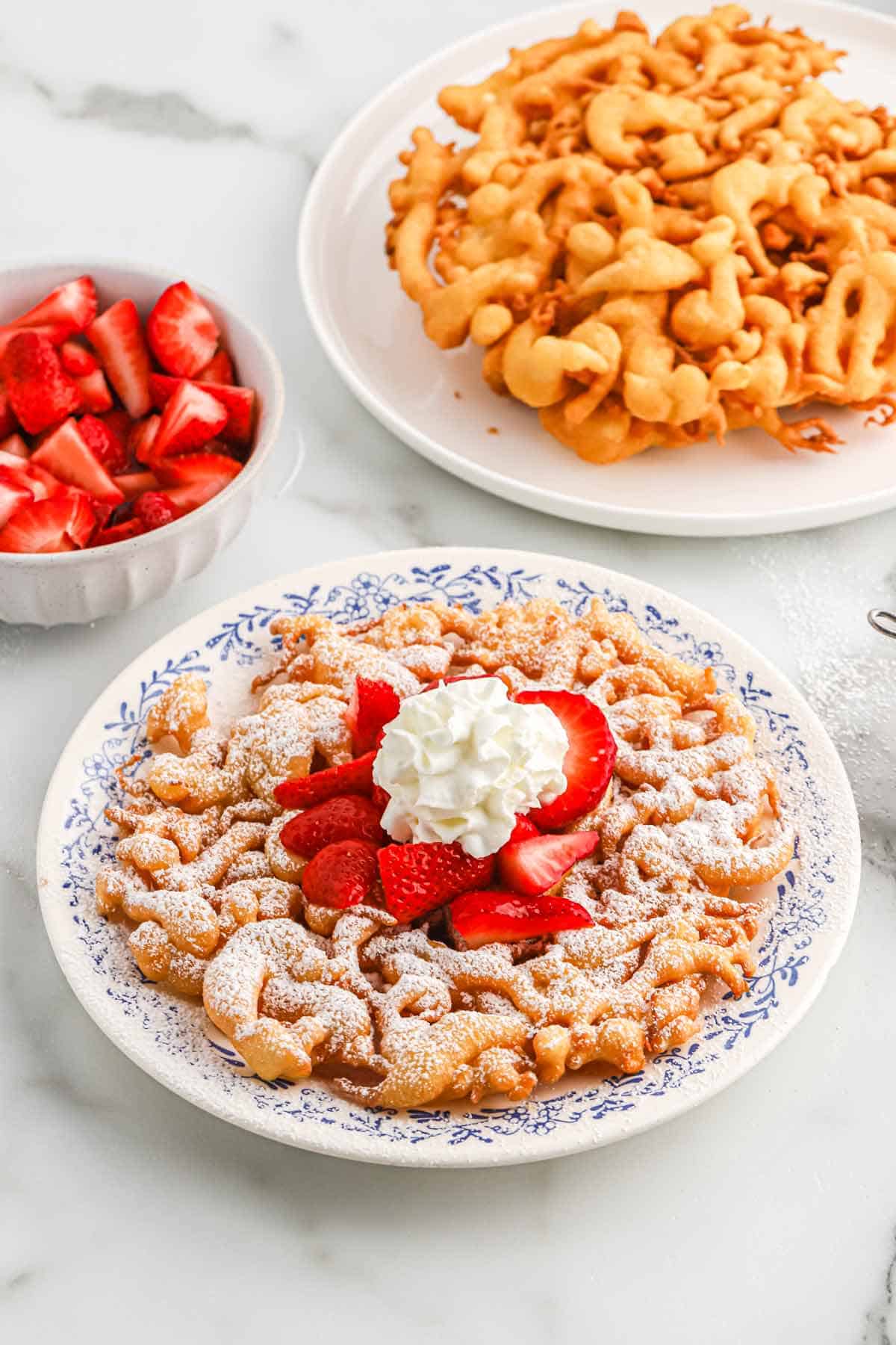 Funnel cake served up sprinkled with powdered sugar, whipped cream and fresh berries.