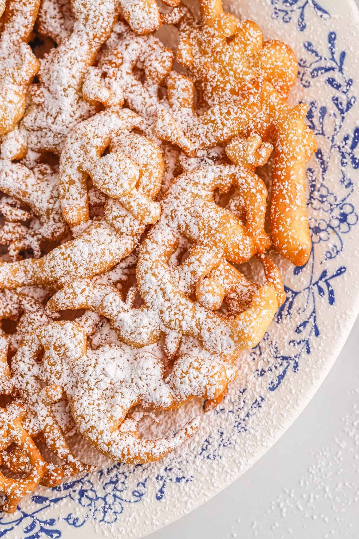 A close up of a funnel cake on a plate sprinkled with powdered sugar.