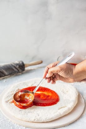 Marinara sauce being spread on Neapolitan pizza dough from scratch