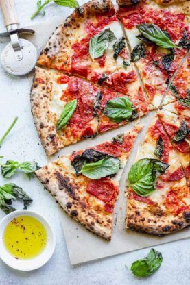 A close up of Neapolitan margherita pizza fresh out of the oven with basil, marinara and mozzarella
