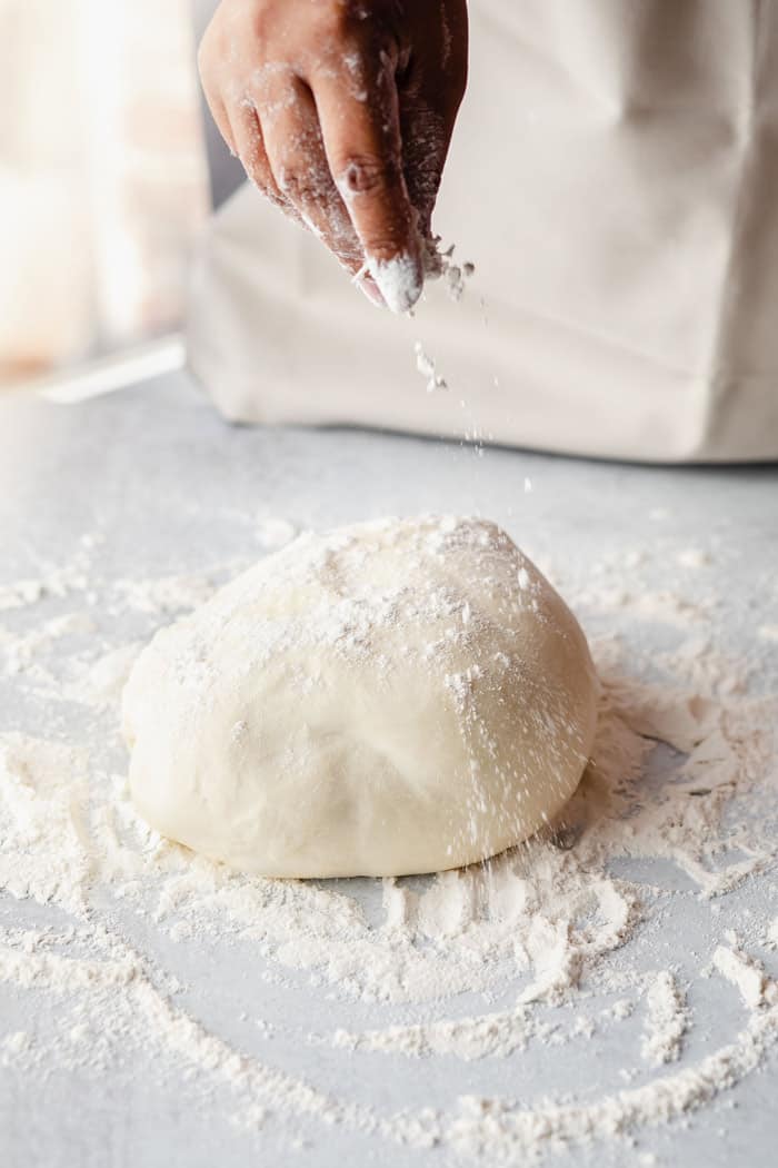 All purpose flour being sprinkled on pizza dough before being rolled out