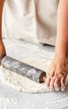 After learning how to make pizza dough, a woman is rolling it out with a rolling pin to prepare for baking