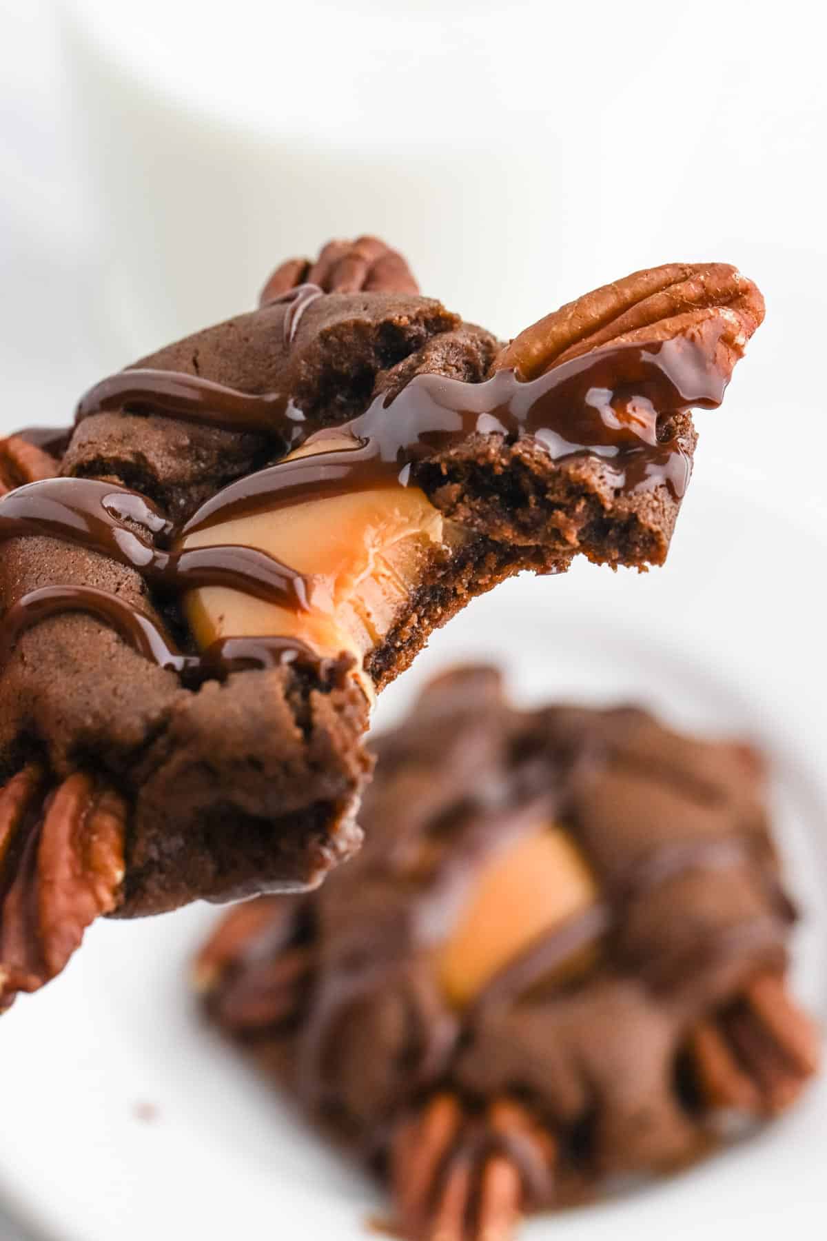 A chocolate turtle cookie up over the plate of more cookies with a bite missing to show caramel inside.