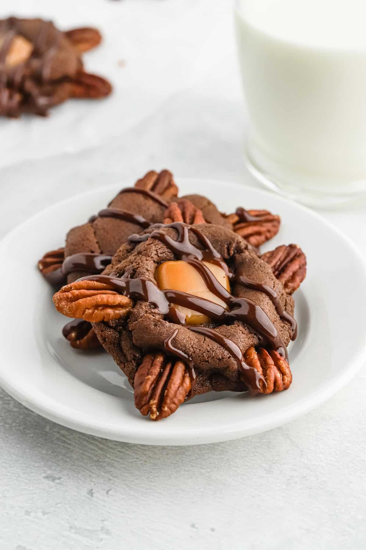 Chocolate turtle cookies on a small plate with a glass of milk.
