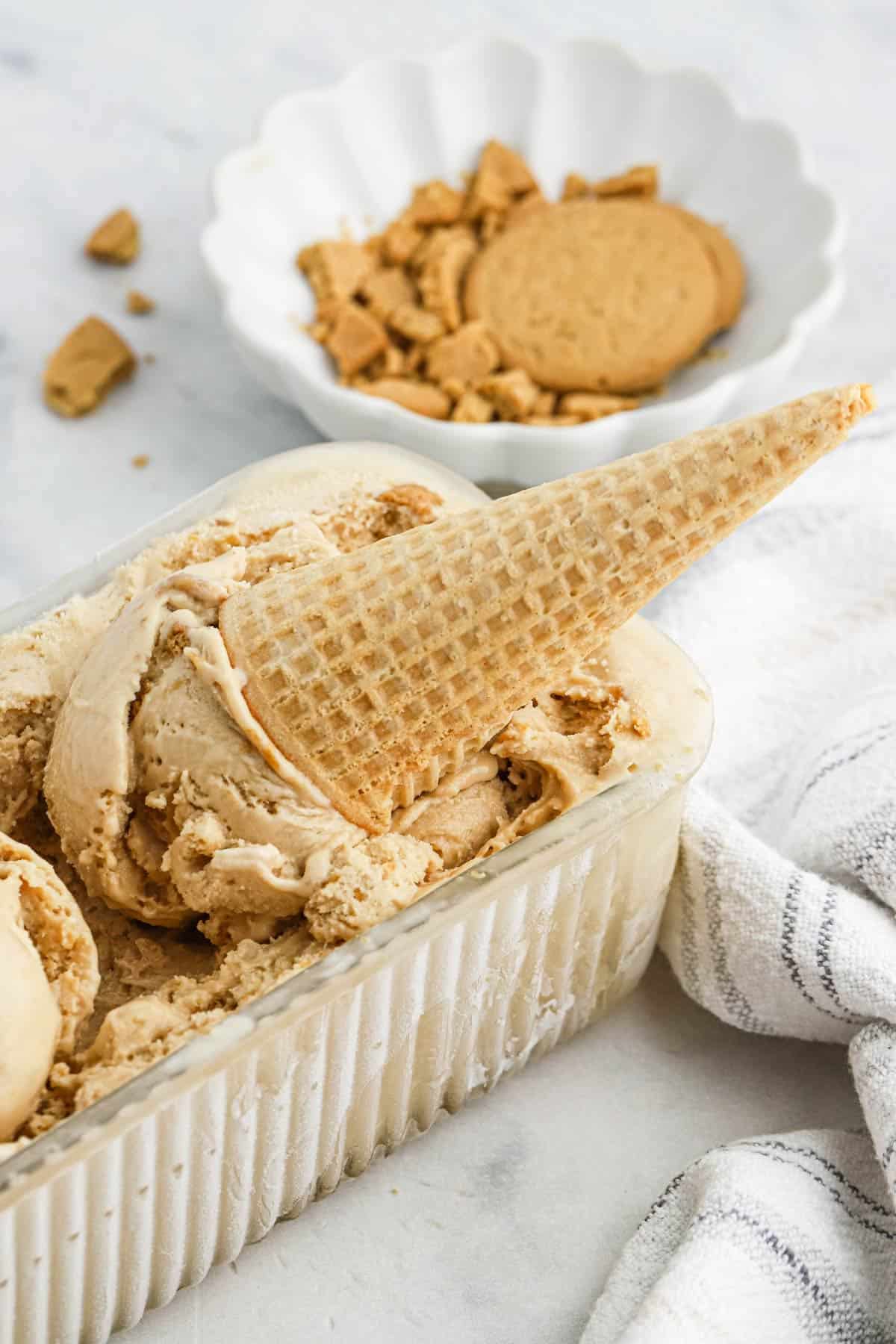 Cookie butter ice cream in a loaf pan with a scoop on top in a cone.