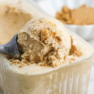 Cookie butter ice cream in a container with a utensil scooping up some to serve.