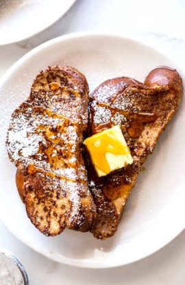 Two slices of french toast on a white plate with butter and maple syrup