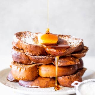 Syrup drizzling down a high stack of eggnog french toast on a white plate