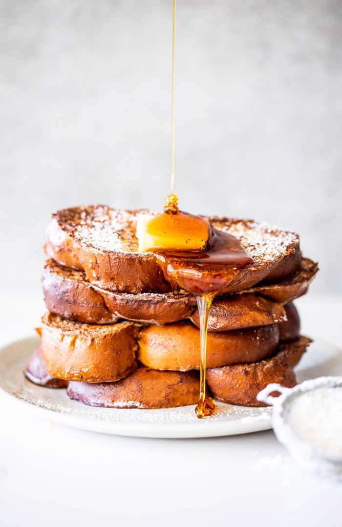 Syrup drizzling down a high stack of eggnog french toast on a white plate
