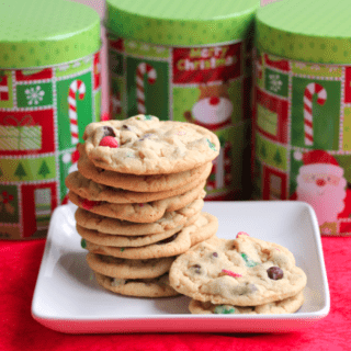 A stack of Christmas chip cookies on a square, white plate with Christmas decorated metal tins in the background